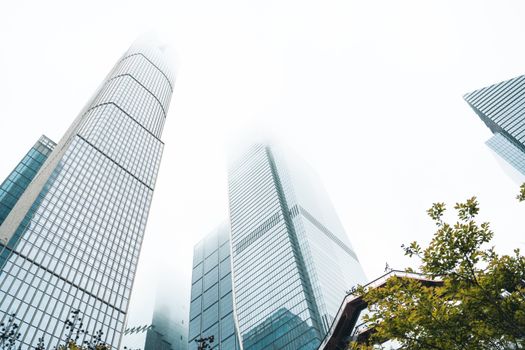 Low-angle view of modern skyscrapers disappearing into the foggy sky, capturing urban architecture.