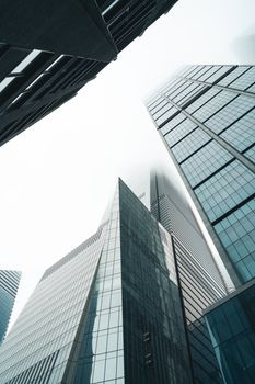 Low-angle view of modern skyscrapers towering into a foggy sky, illustrating urban architecture.