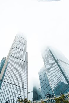 Low angle shot of tall skyscrapers disappearing into foggy clouds against a bright sky.