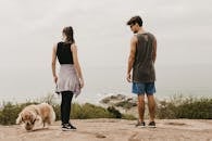 Man and Woman Standing on Brown Rock Near White Dog