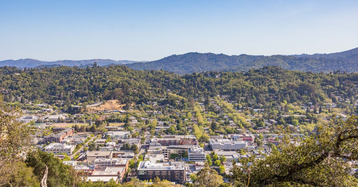 Aerial view of a town with lush hills and clear sky, capturing urban and natural beauty.