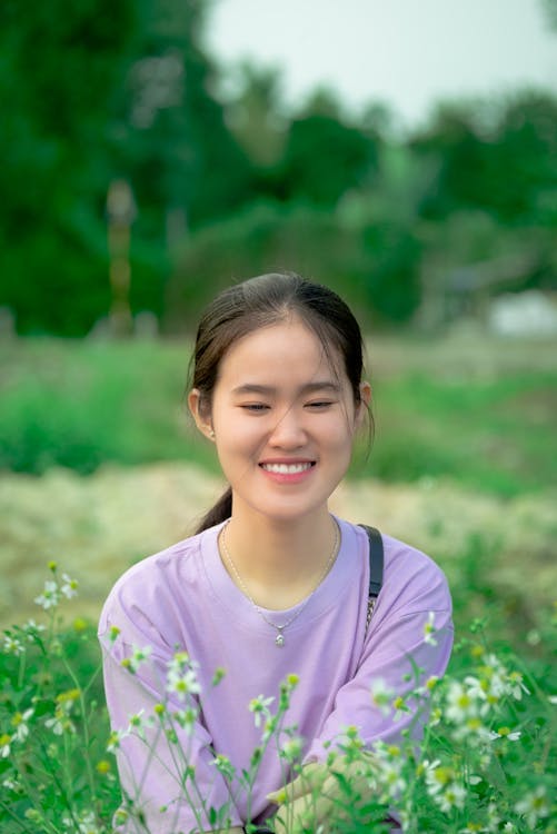Free Smiling Woman in Purple Shirt Standing Near White Flowers Stock Photo