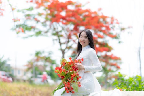 Woman in White Traditional Dress Holding Red Flowers