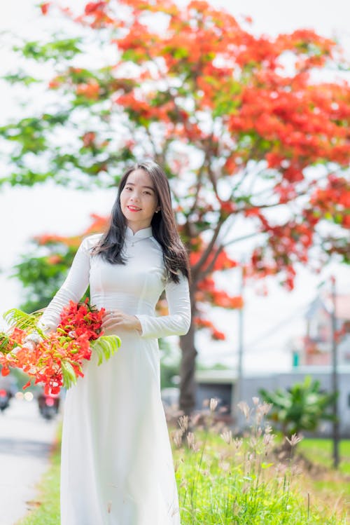 Woman in White Traditional Dress Holding Red Flowers