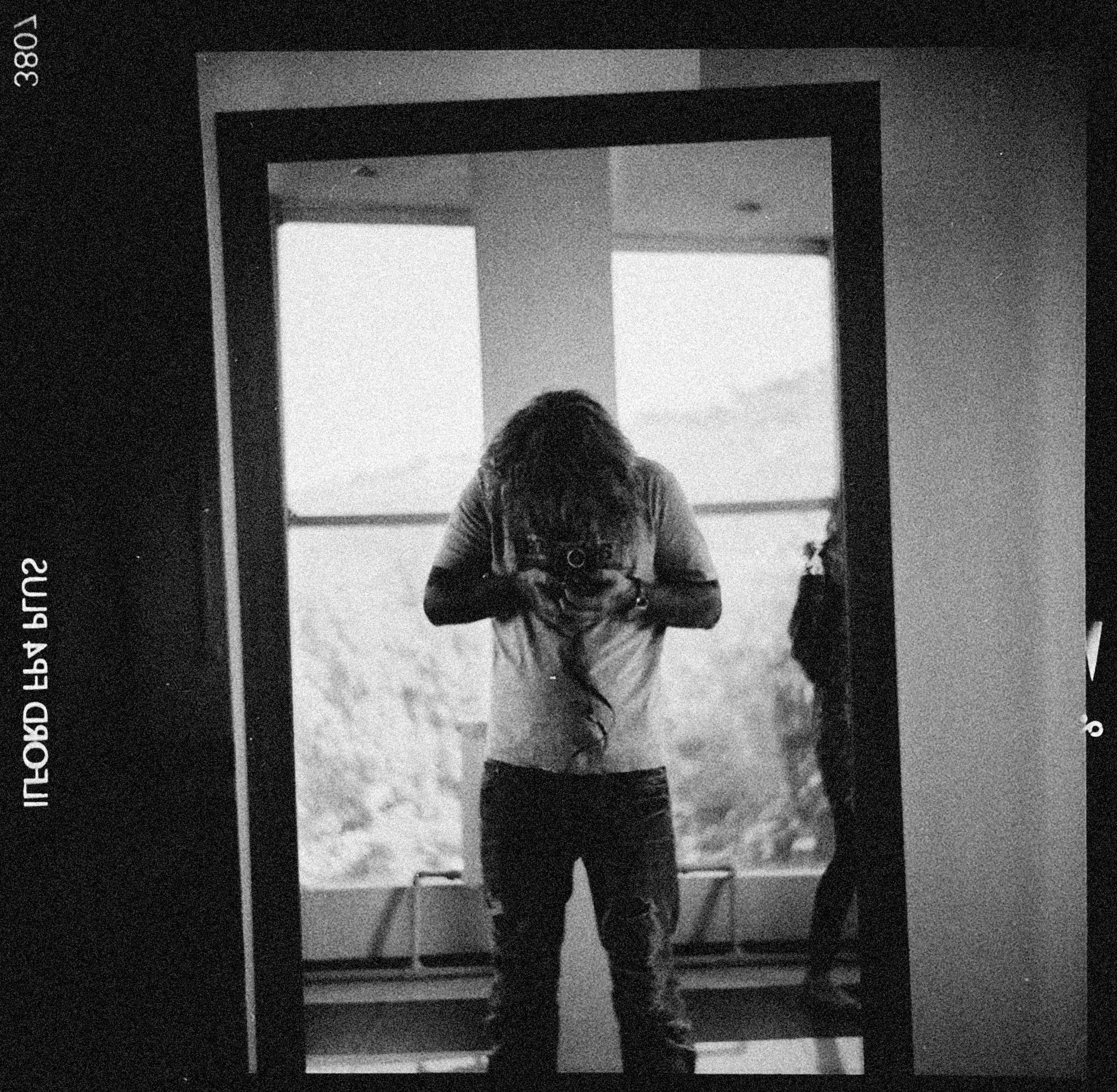 Black and white photo of a person taking a picture in front of a mirror, creating an artistic reflection.