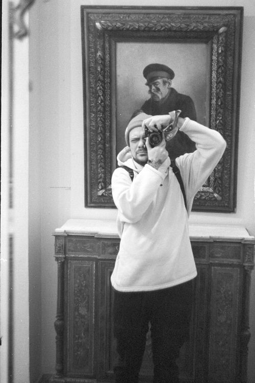 Free A monochrome photograph of a man capturing a self-portrait in front of a framed painting indoors. Stock Photo