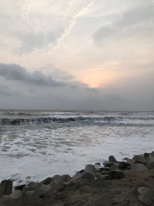 Free Peaceful ocean waves rolling onto a rocky shore under a cloudy sky at sunset. Stock Photo