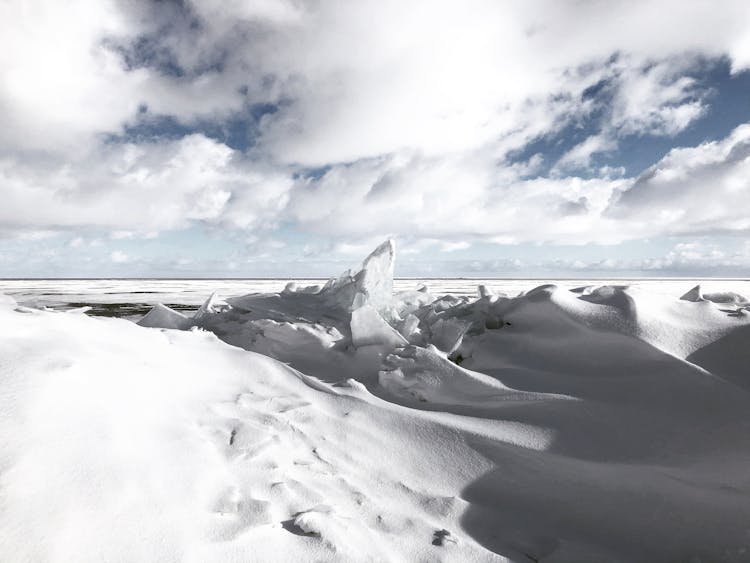 Snow Covered Land Near A Body Of Water Under Blue Sky And White Clouds