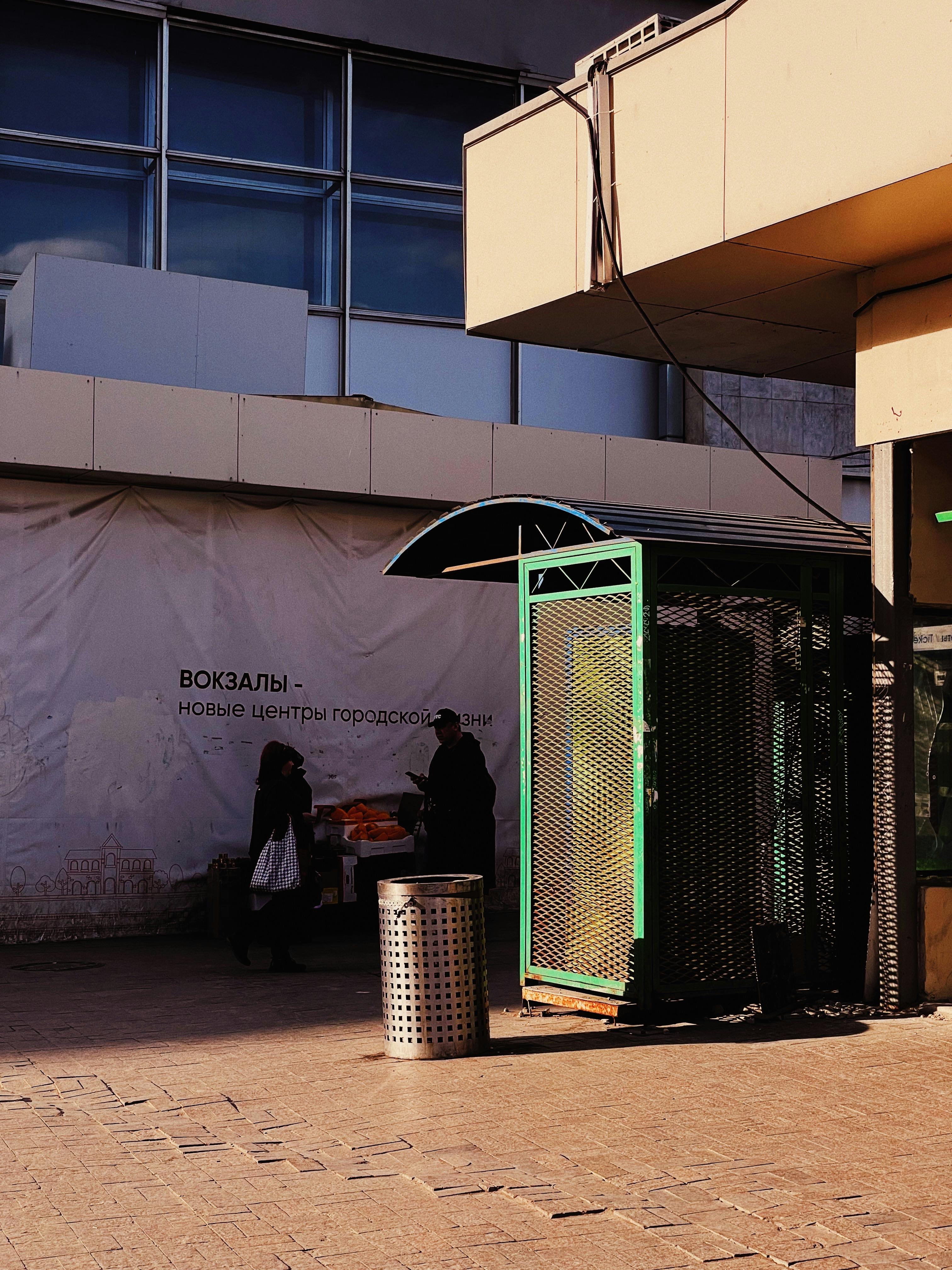 Free Silhouette of street vendors against urban building facade in bright sunlight. Stock Photo