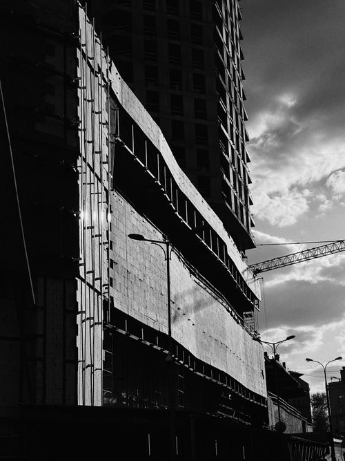 Free Black and white photo of a high-rise building under construction with a crane and dramatic sky. Stock Photo