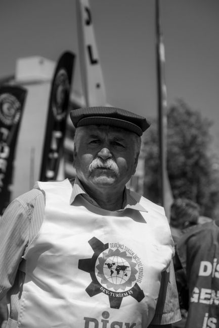 Black and white photo of an elderly man in a protest wearing a vest with an organization logo.