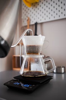 Close-up view of pour-over coffee brewing with glass carafe and digital scale indoors.
