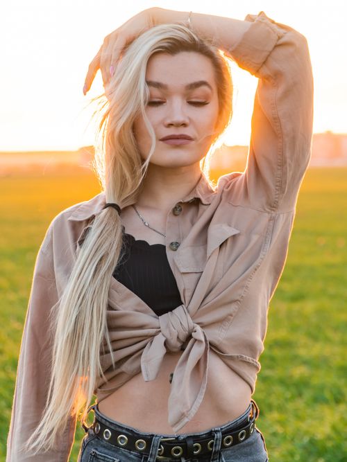 Free Portrait of a young woman with long hair posing outdoors at sunset, wearing casual stylish attire. Stock Photo