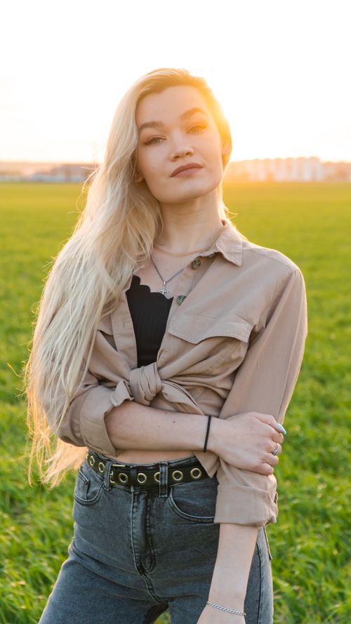 Free A confident blonde woman poses in a sunlit green field, showcasing casual fashion. Stock Photo