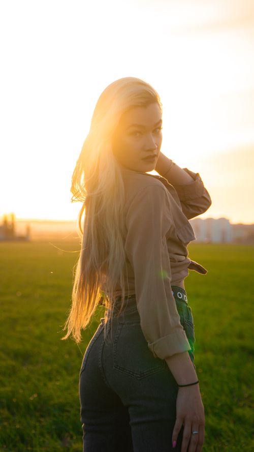 Free A captivating portrait of a blonde woman standing gracefully in a sunlit field at sunset. Stock Photo
