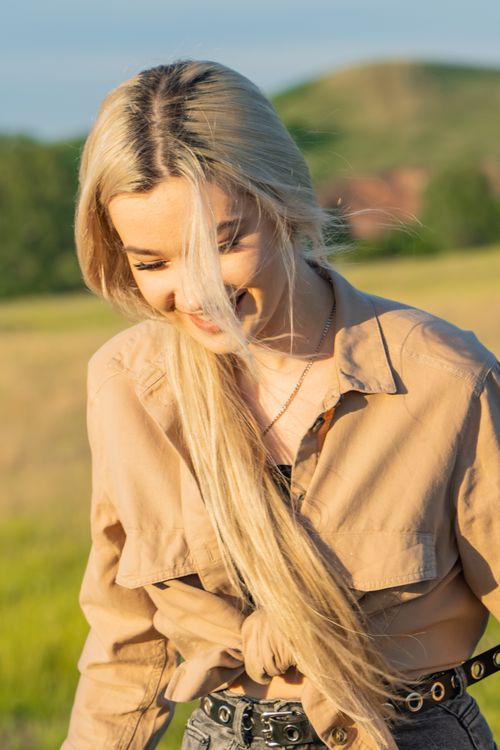 Free Joyful blond woman smiling under the sun in a serene outdoor setting. Stock Photo