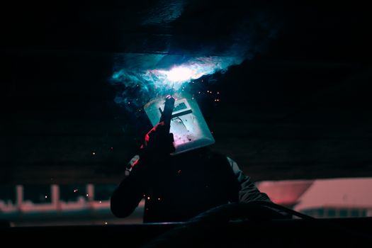 Silhouette of a welder working with sparks flying and smoke, showcasing safety gear.