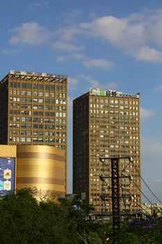 Two tall brown office buildings with signage under a clear blue sky.