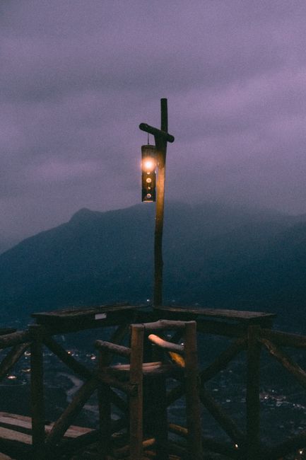 A moody evening scene with a lantern on a wooden balcony overlooking foggy mountains.