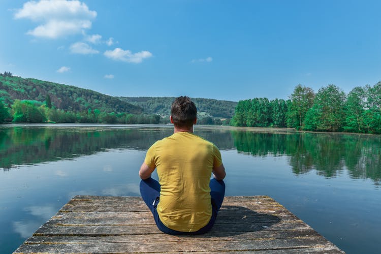 Man Sitting On The Dock Near A Lake