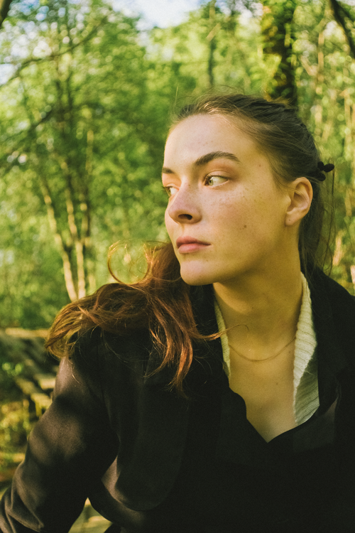 Free Young woman in a serene forest setting, deep in thought, wearing a black sweater. Stock Photo