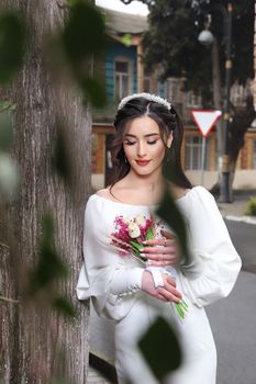 A woman in a stylish white dress holds a vibrant floral bouquet against an outdoor background.