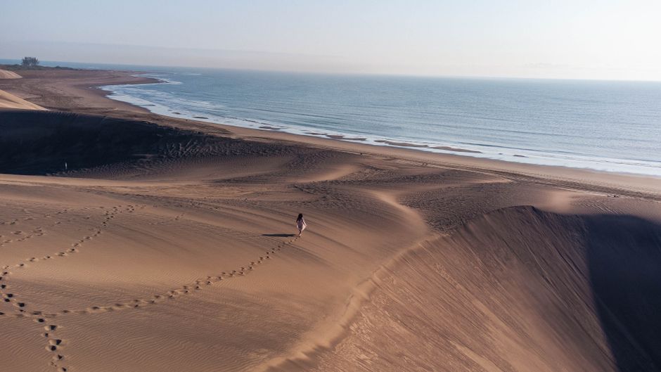 A person walks alone on vast sand dunes next to the ocean at Playa del Carmen, Mexico.