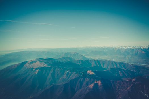 A breathtaking aerial view of a vast mountain range enveloped in mist under a clear sky.