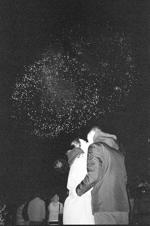 Grayscale Photo of Couple Kissing During Fireworks Display