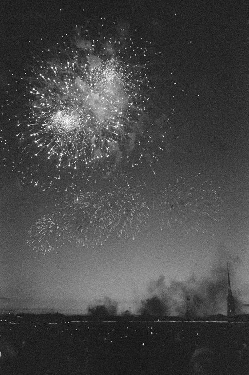 Free Grayscale image capturing fireworks illuminating the night sky above a distant cityscape. Stock Photo