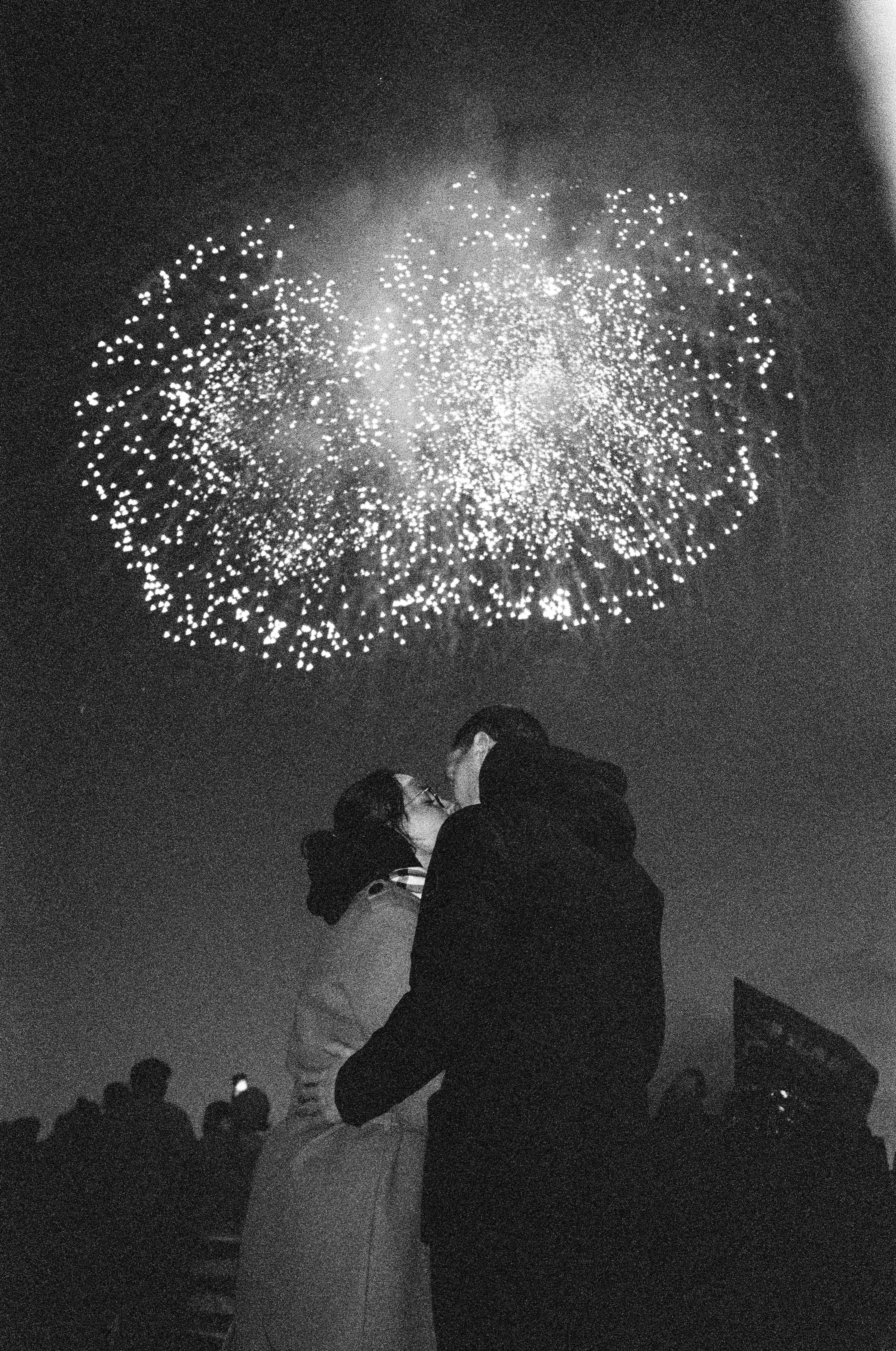 A couple embracing and kissing beneath a spectacular fireworks show at night.