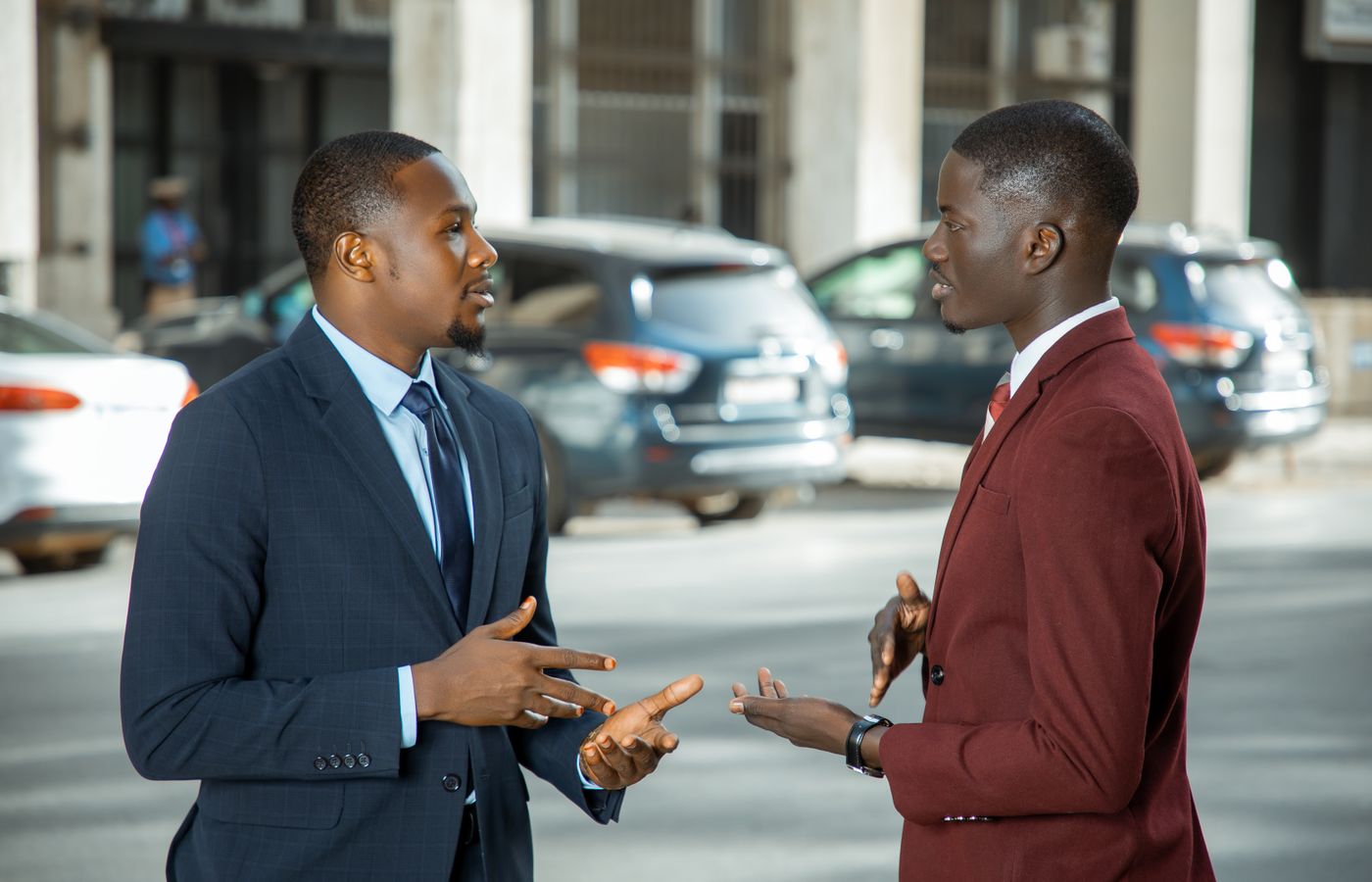 Two African businessmen in formal suits have a discussion on a city street in Dakar, Senegal.