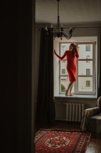 Woman stands in a red dress on a windowsill in a stylish urban apartment.