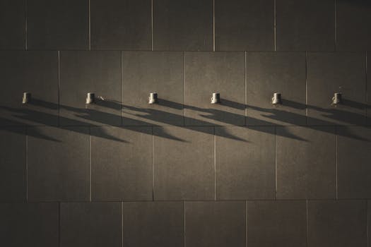 Artistic view of long shadows cast by metal hooks on a tiled wall.
