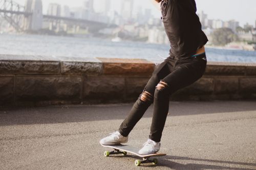 Free A skateboarder rides near a city waterfront with a bridge in the background. Stock Photo