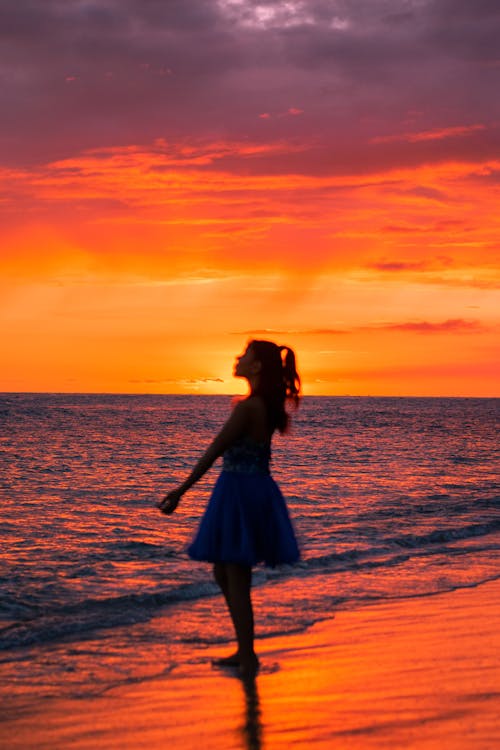 Tourist in a Blue Dress on the Beach at Sunset