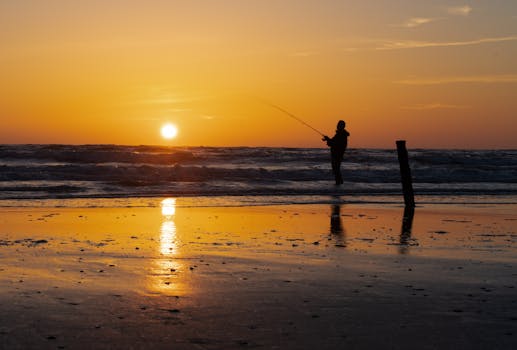 A fisherman silhouette casting a line against a stunning beach sunset.