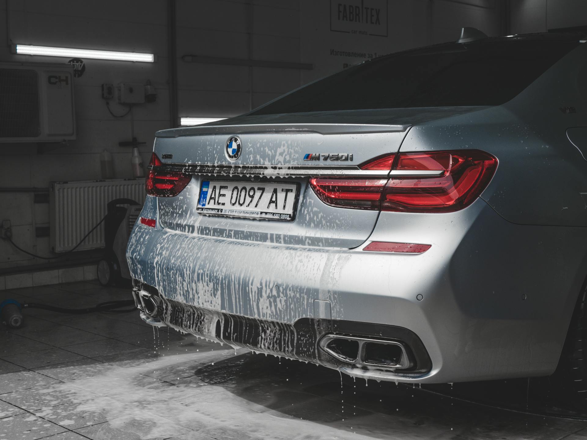 Back view of a luxury BMW car being washed, showcasing taillights and exhaust.