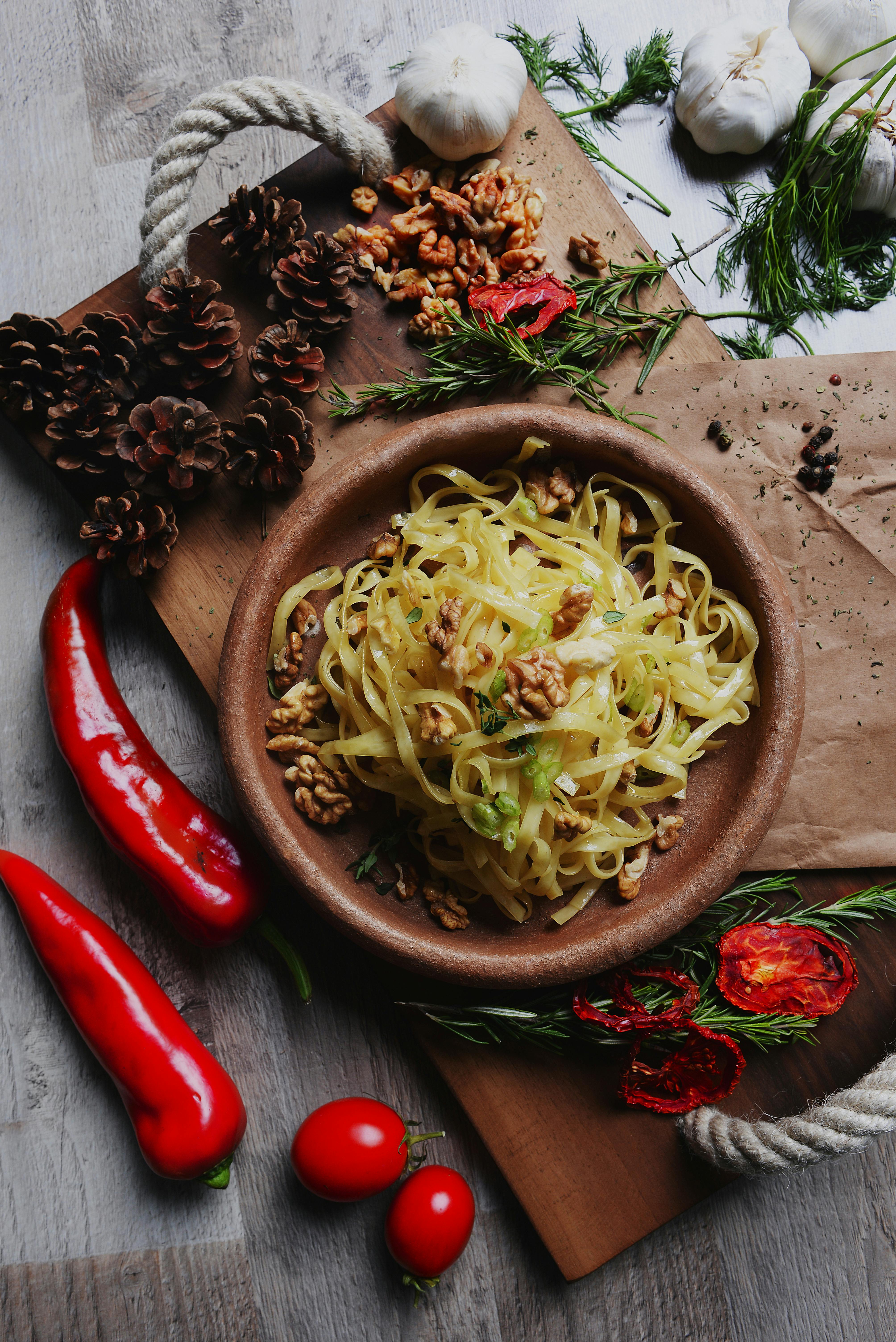 Delicious pasta served with walnuts and fresh herbs, surrounded by chili peppers and tomatoes.