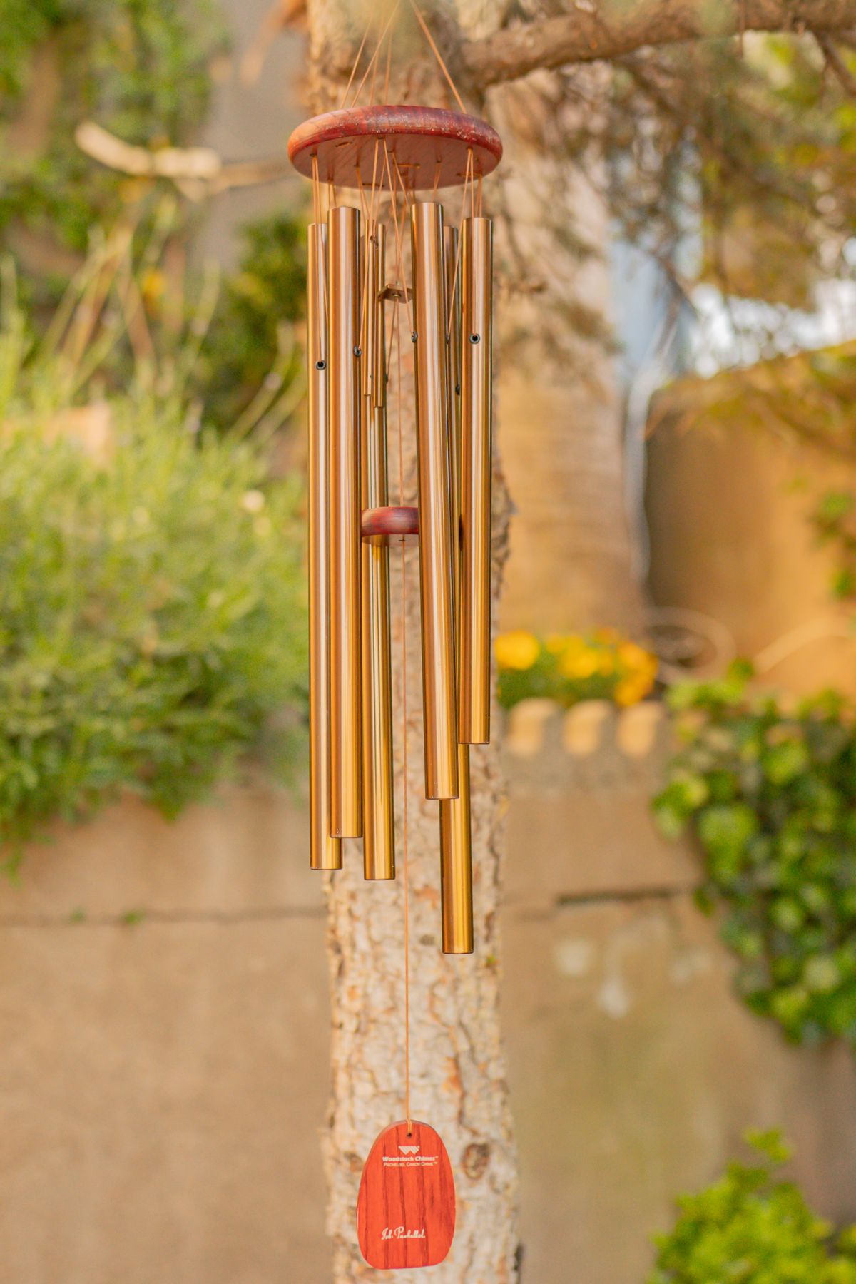 A handmade wind chime hanging outdoors surrounded by greenery