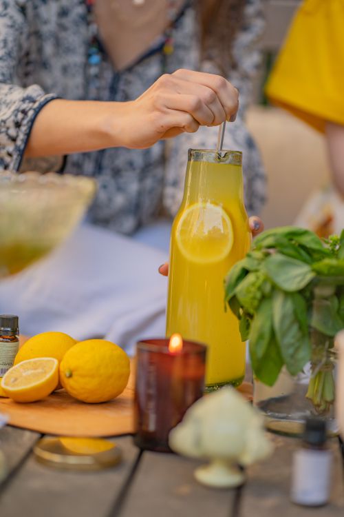 Free A scene of a person stirring homemade lemon juice outdoors, featuring vibrant lemons and fresh herbs. Stock Photo