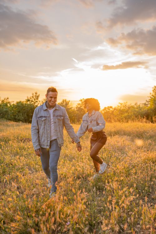 Free A happy couple holding hands and enjoying a romantic walk in a sunlit meadow at sunset. Stock Photo