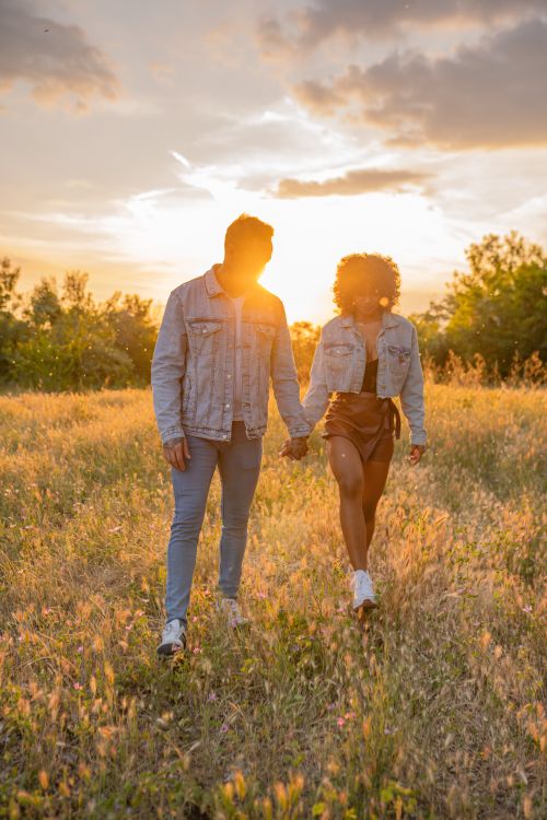 Free A fashionable couple holding hands walking through a field at sunset, exuding love and happiness. Stock Photo