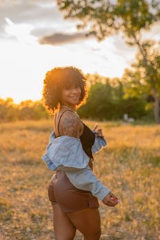 Smiling woman enjoying a summer evening in a sunlit meadow, exuding happiness and warmth.