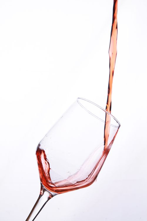 Free A dynamic shot of red wine being poured into a wine glass against a white backdrop. Stock Photo