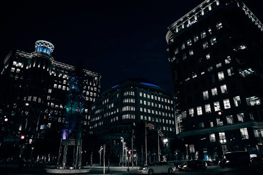 Dramatic night scene of illuminated office buildings in a bustling downtown area.