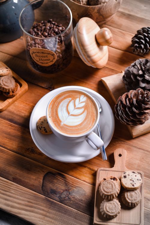 Free Cozy setup featuring a latte with art, cookies, and coffee beans in a rustic setting. Stock Photo