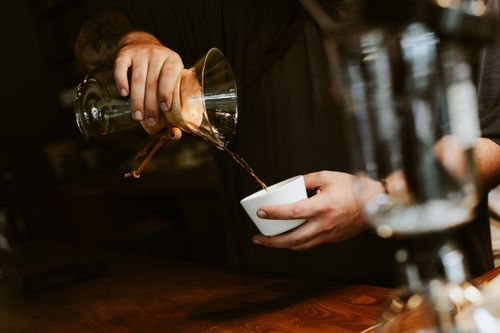 Free A barista pouring coffee into a cup using a Chemex brewer in a cozy café setting. Stock Photo
