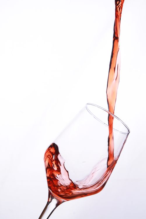 Free Dynamic shot of red wine gracefully pouring into a tilted wine glass against a white backdrop. Stock Photo