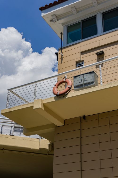 Free View of a lifebuoy on a hotel balcony against a vibrant blue sky and clouds, suggesting safety and vacation vibes. Stock Photo